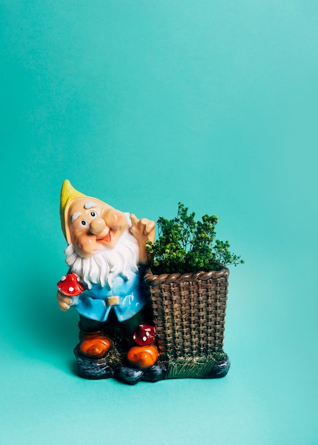 Dwarf figurine with show plant in the basket against colored backdrop