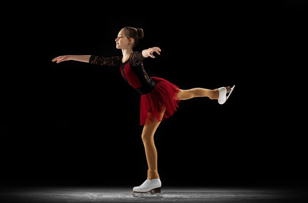 黒の背景に分離された若い女の子の子供のフィギュアスケート選手のトレーニングのダイナミックな肖像画