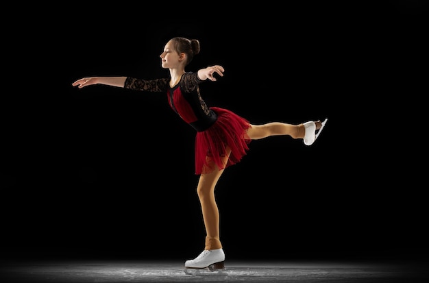 검정 배경 위에 격리된 어린 소녀 피겨 스케이팅 선수 훈련의 역동적인 초상화