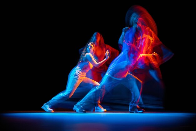 Dynamic portrait of young man and woman dancing hiphop isolated over black background with mixed lights effect