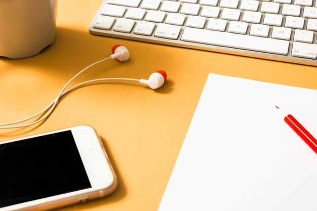 Earphone; keyboard; paper; red pencil and cellphone on an orange background