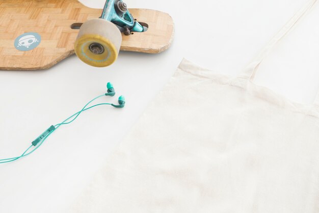 Earphone, skatingboard and handbag on white background