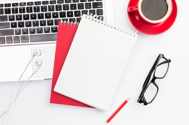 Earphones and spiral notepads on laptop with coffee cup and eyeglasses