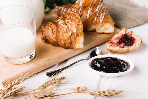 Ears of wheat, milk glass, and berries jam with croissant on the table