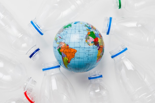 Earth globe surrounded plastic bottles on grey table