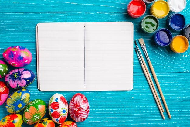 Easter background with blank notebook and paint brushes