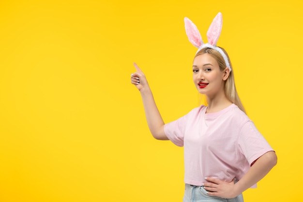 Easter beautiful cute blonde girl with bunny ears pointing up and smiling