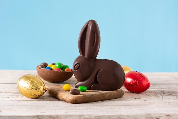 Easter chocolate bunny and colorful eggs on wooden table and blue background