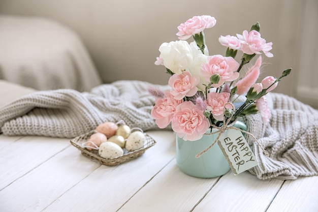 Easter composition with fresh flowers in a vase, a knitted element and the inscription Happy Easter on the card.