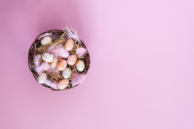 Пасхальная композиция с традиционным декором. маленькие декоративные красочные яйца и мягкие перья в плетеной корзине на розовом светлом фоне.