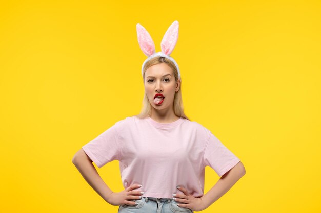 Easter cute young blonde girl wearing pink bunny ears making funny face with the tongue out