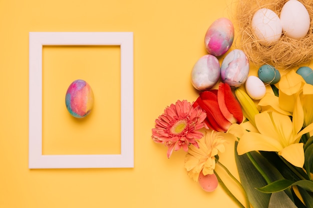 Foto gratuita la struttura del confine dell'uovo di pasqua con i fiori freschi e le uova annidano su fondo giallo