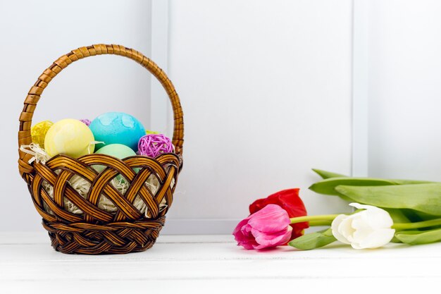 Easter eggs in basket with tulips and blank frame on table 