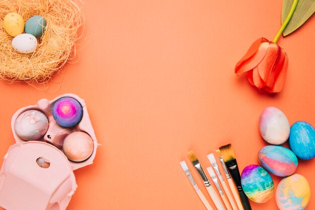 Easter eggs; carton; paint brushes and red tulip on an orange backdrop