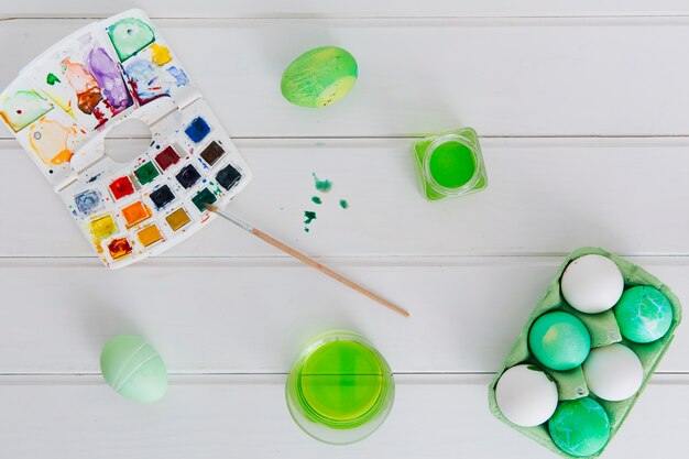 Easter eggs in container between cups with dye liquid near brush with set of colors