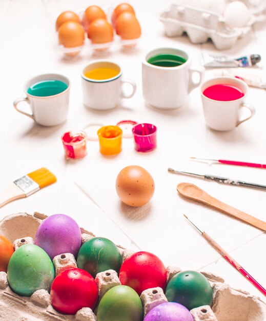 Easter eggs in container near brushes and dye liquid in cups