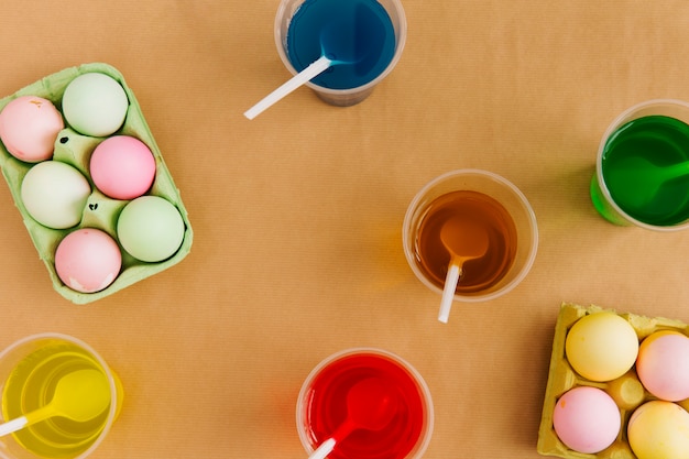 Easter eggs in containers near cups with colourful dye liquid