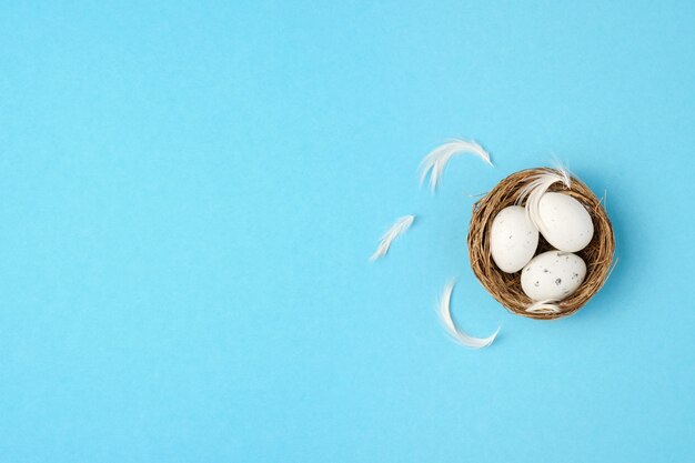 Пасхальные яйца, перья в гнезде на синем фоне. минимальная концепция, вид сверху. скопируйте пространство.