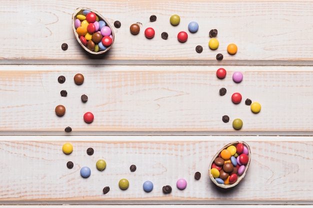 Easter eggs filled with colorful candies on wooden desk with space in the center for writing the text