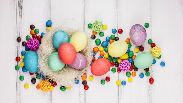 Бесплатное фото Пасхальные яйца в гнезде с конфетами на деревянном столе