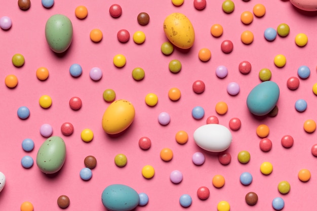 Easter eggs and multicolored gem candies against pink background