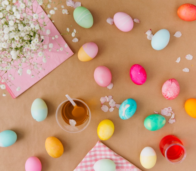Пасхальные яйца возле чашек с красителем, салфетками и цветами
