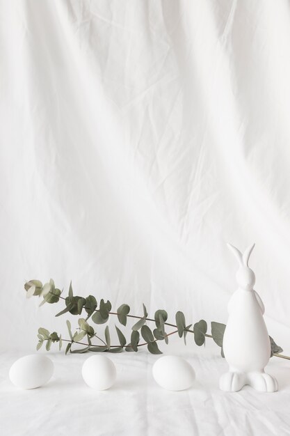 Easter eggs near plant twigs and figure of rabbit