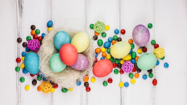 Easter eggs in nest with candies on wooden table