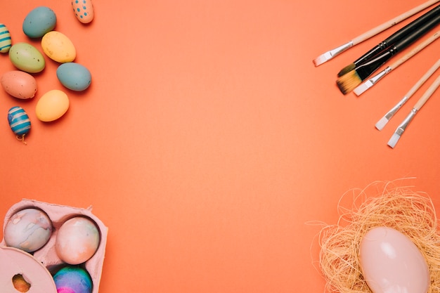 Easter eggs; paint brushes; egg nest on the corner of the orange background