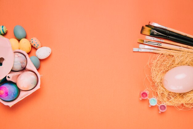 Free photo easter eggs; paint brushes; egg nest on the corner of the orange background