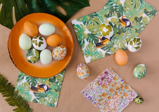 Easter eggs on plate near napkins with tropical paints and leaves