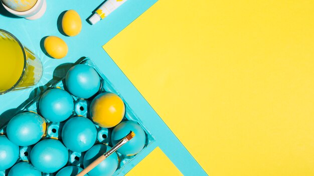 Easter eggs in rack with paint brush and paper on blue table