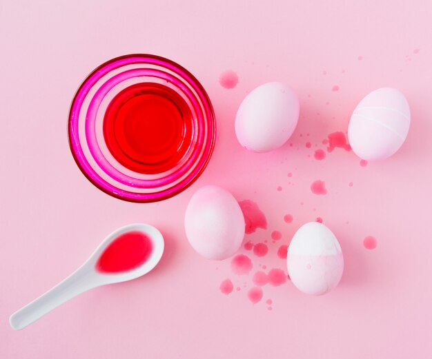 Easter eggs between splashes near bowl and spoon with dye liquid