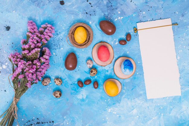 Easter eggs with paper and flowers on table