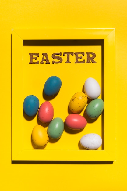 Foto gratuita iscrizione di pasqua nel telaio con uova colorate sul tavolo giallo