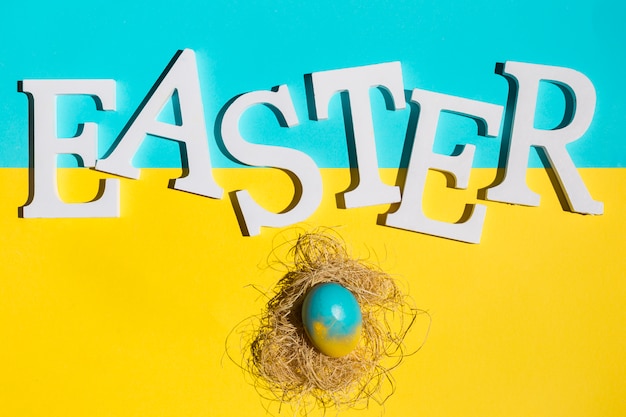 Бесплатное фото Пасхальная надпись с цветным яйцом с сеном на столе