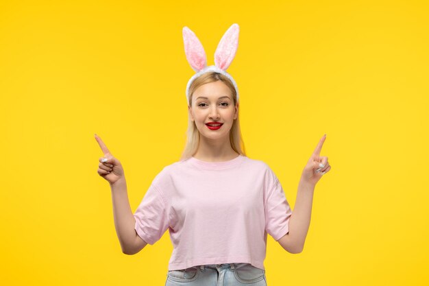 Easter lovely blonde adorable girl with pink bunny ears and red lipstick smiling and pointing up