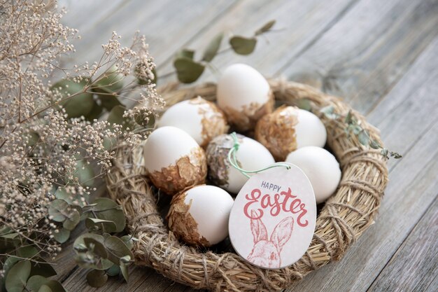 Пасхальный натюрморт с украшенными пасхальными яйцами и декоративным гнездом на деревянной поверхности с сухими ветками. Счастливой Пасхи желает концепции.