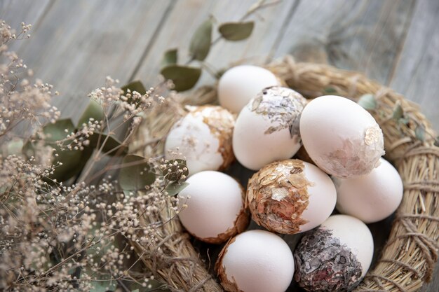 Пасхальный натюрморт с украшенными пасхальными яйцами и декоративным гнездом на деревянной поверхности с сухими веточками