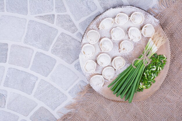 Eastern khinkal dough with minced herbs and onion bunch on wooden board.