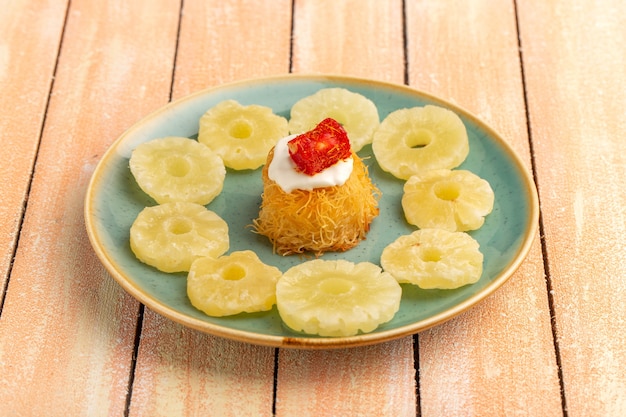 восточное печенье внутри тарелки с белыми кремовыми сушеными ананасовыми кольцами на деревянном столе