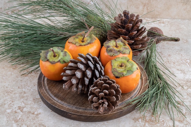 Eastern persimmons and conifer cones bundle together on marble surface.