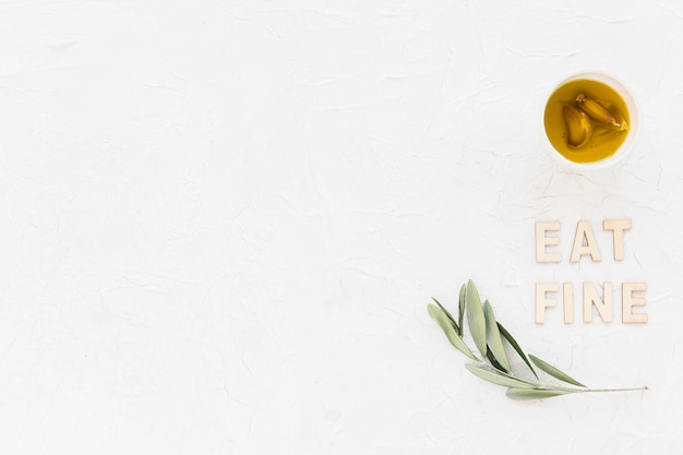 Eat fine text with olive twig and garlic clove oil in bowl on white backdrop