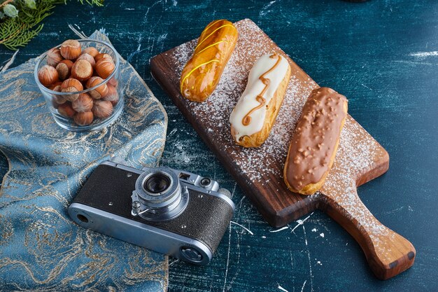 Eclairs with berry sauces on a wooden board. 