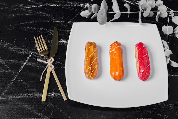 Eclairs with colorful syrups in a white plate.