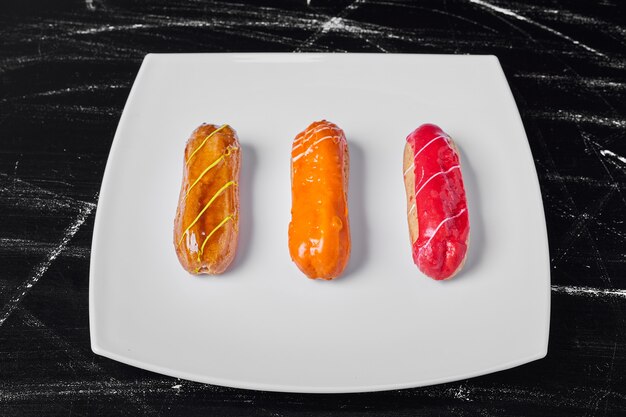 Eclairs with colorful syrups on a white platter.