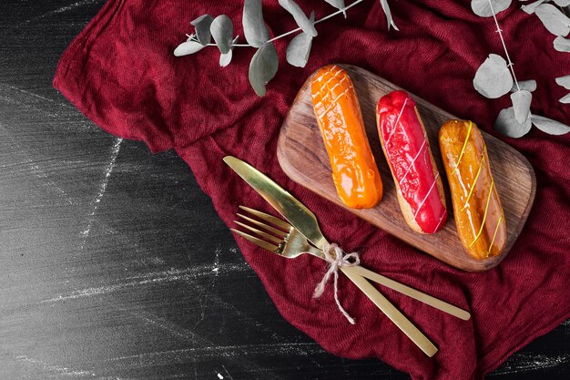 Eclairs with colorful syrups on a wooden board.