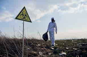 Free photo ecologist standing in field with garbage and biohazard sign