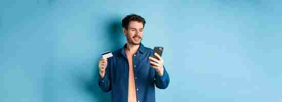 Free photo ecommerce concept image of handsome caucasian man paying online looking at mobile phone screen and h