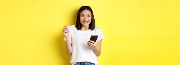 전자 상거래 및 온라인 쇼핑 개념 스마트 폰을 들고 인터넷에서 지불하는 쾌활한 아시아 소녀